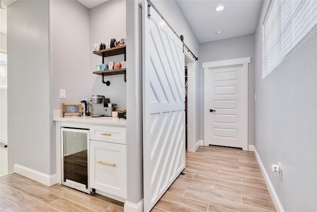 bar featuring wine cooler, baseboards, light wood-style flooring, and a barn door