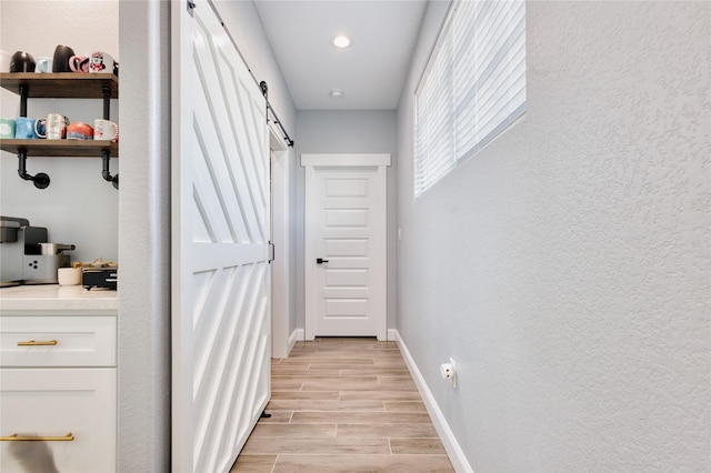 corridor featuring light wood-style floors, a barn door, baseboards, and recessed lighting