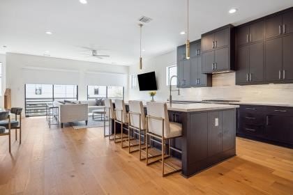 kitchen featuring decorative backsplash, a kitchen breakfast bar, a center island with sink, decorative light fixtures, and light wood-type flooring