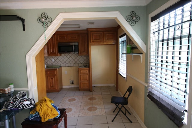 kitchen featuring brown cabinets, backsplash, stainless steel microwave, and light tile patterned floors