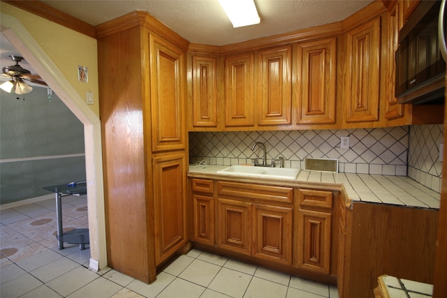 kitchen featuring tasteful backsplash, ceiling fan, tile countertops, light tile patterned floors, and sink