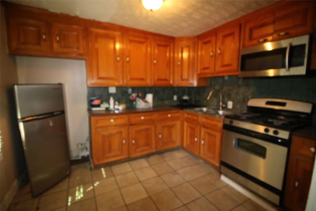 kitchen featuring dark countertops, brown cabinetry, light tile patterned flooring, tasteful backsplash, and appliances with stainless steel finishes