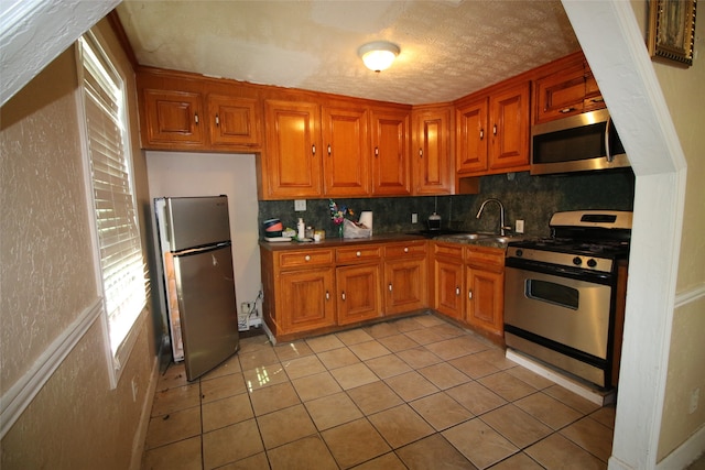 kitchen with appliances with stainless steel finishes, sink, a textured ceiling, decorative backsplash, and light tile patterned floors