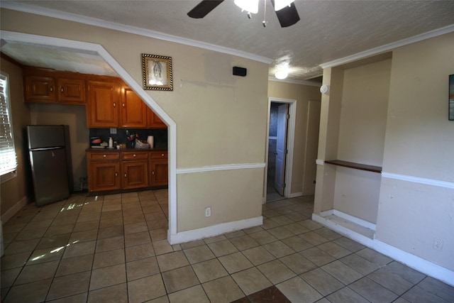 interior space featuring light tile patterned floors, freestanding refrigerator, brown cabinets, ceiling fan, and ornamental molding