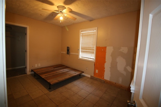 unfurnished bedroom featuring electric panel, tile patterned floors, a textured ceiling, baseboards, and a ceiling fan