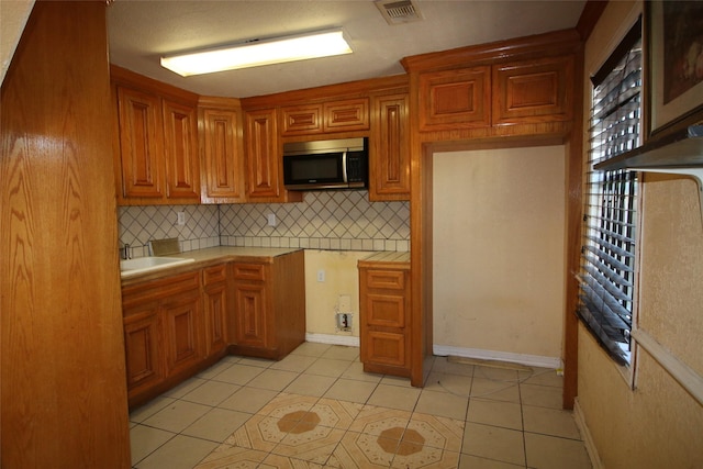 kitchen with a sink, stainless steel microwave, tasteful backsplash, visible vents, and light countertops