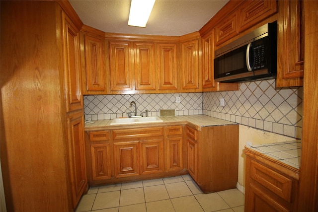 kitchen featuring tile counters, light tile patterned floors, stainless steel microwave, a sink, and decorative backsplash