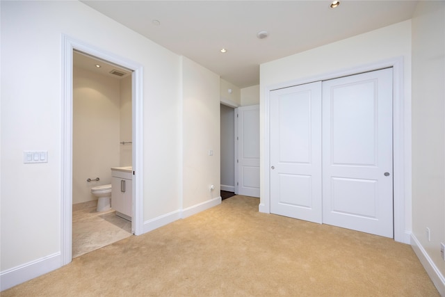 unfurnished bedroom with light colored carpet, a closet, and ensuite bathroom