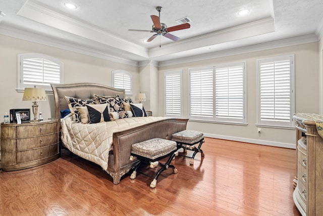 bedroom with a tray ceiling, ornamental molding, multiple windows, and wood-type flooring