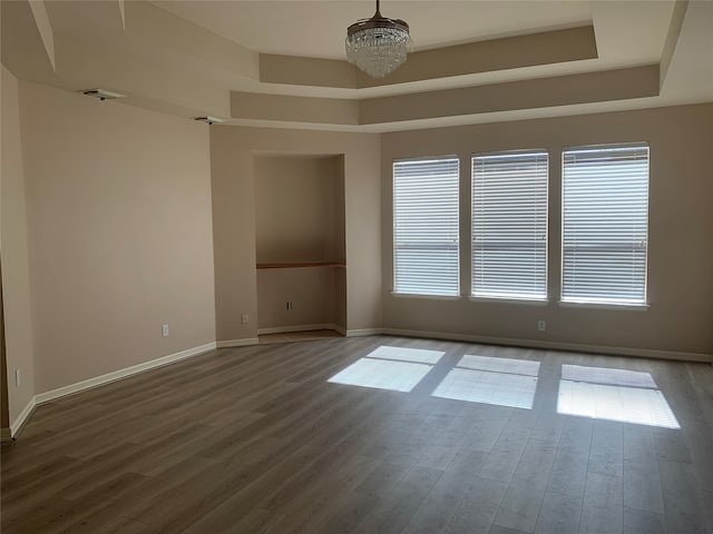 spare room with a tray ceiling, a chandelier, and hardwood / wood-style flooring