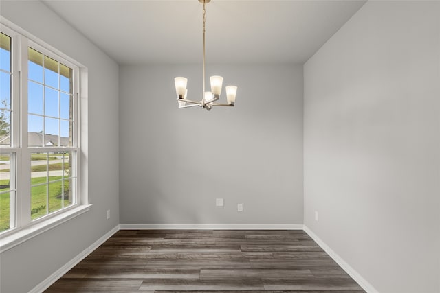 empty room featuring dark wood-type flooring, a healthy amount of sunlight, and an inviting chandelier