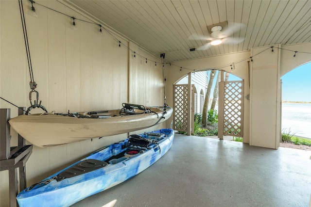 garage with ceiling fan, a water view, and wooden walls