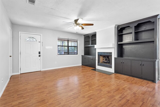 unfurnished living room with a textured ceiling, wood-type flooring, built in features, and ceiling fan