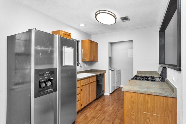 kitchen featuring a textured ceiling, washing machine and clothes dryer, light wood-type flooring, sink, and stainless steel appliances