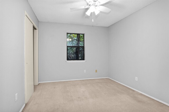 unfurnished bedroom with a textured ceiling, light colored carpet, a closet, and ceiling fan