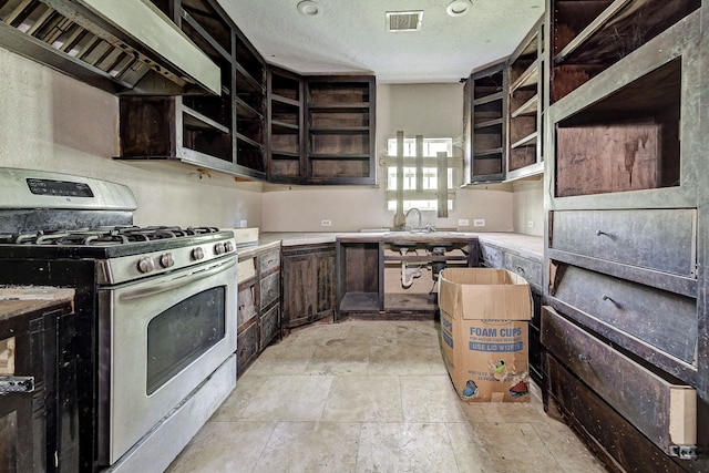 kitchen with wall chimney range hood, dark brown cabinets, a textured ceiling, and stainless steel gas range