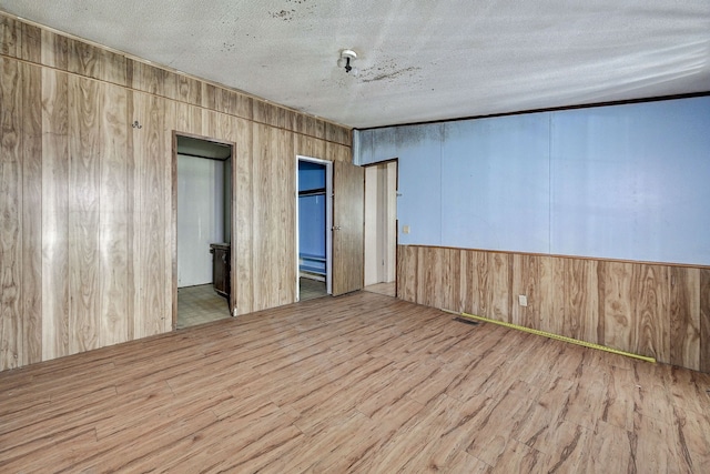 unfurnished room featuring wood walls, a textured ceiling, and light wood-type flooring