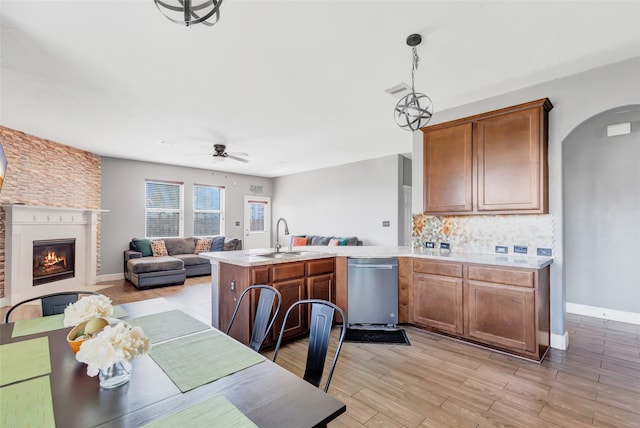 kitchen with dishwasher, light hardwood / wood-style flooring, hanging light fixtures, sink, and a fireplace