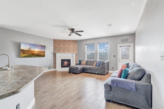 living room featuring a large fireplace, sink, light hardwood / wood-style floors, and ceiling fan