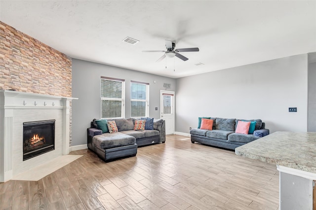 living room with ceiling fan, a stone fireplace, and light hardwood / wood-style flooring