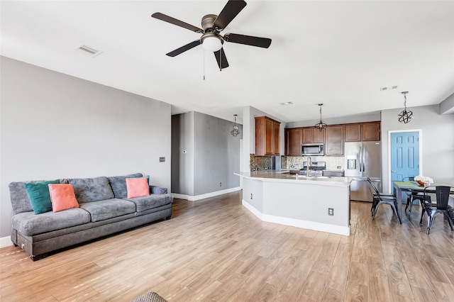 kitchen with hanging light fixtures, stainless steel appliances, backsplash, light hardwood / wood-style floors, and ceiling fan