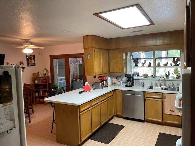 kitchen featuring a textured ceiling, fridge, sink, dishwasher, and kitchen peninsula