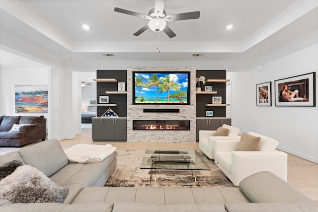 living room featuring a stone fireplace, crown molding, light wood-type flooring, and ceiling fan