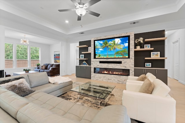 living room featuring a tray ceiling, ornamental molding, a fireplace, and light wood-type flooring