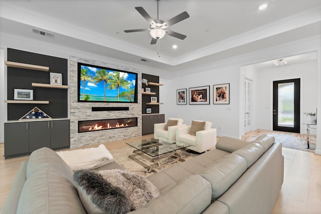 living room with light wood-type flooring, a fireplace, built in features, ceiling fan, and ornamental molding