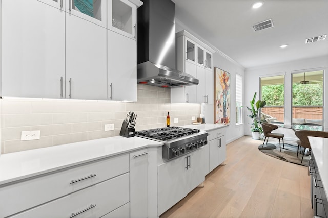 kitchen with wall chimney range hood, stainless steel gas cooktop, backsplash, white cabinets, and light hardwood / wood-style flooring