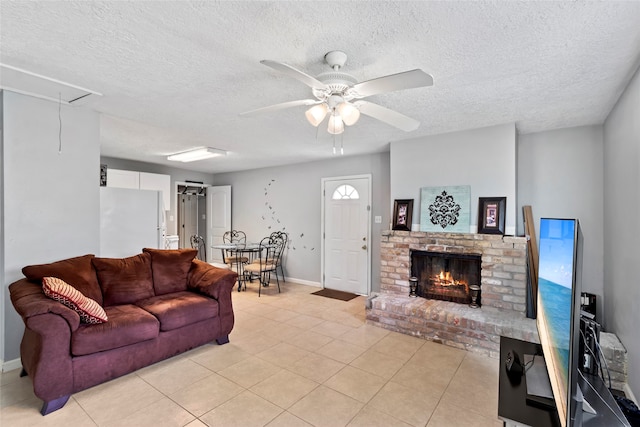 living room featuring a brick fireplace, a textured ceiling, light tile patterned floors, and ceiling fan