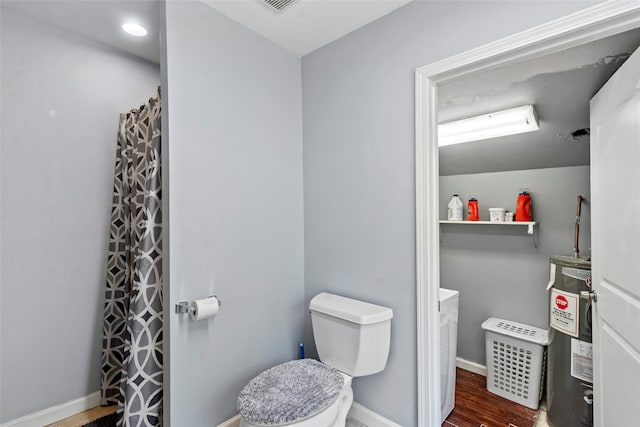 bathroom featuring electric water heater, hardwood / wood-style flooring, and toilet