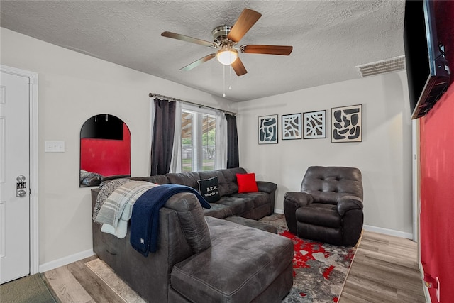 living room featuring ceiling fan, a textured ceiling, and light wood-type flooring