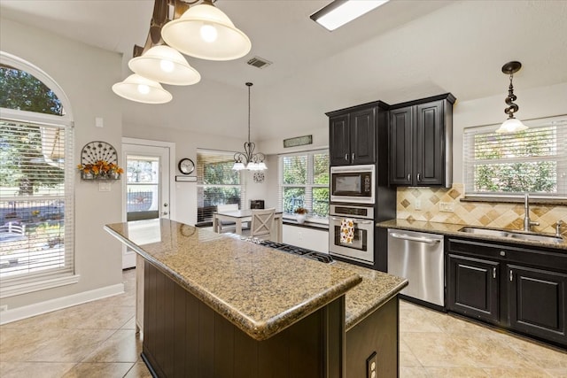 kitchen with sink, stainless steel appliances, tasteful backsplash, light stone counters, and a kitchen island