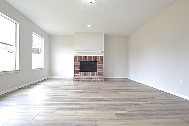 unfurnished living room featuring light hardwood / wood-style floors, a textured ceiling, and a brick fireplace