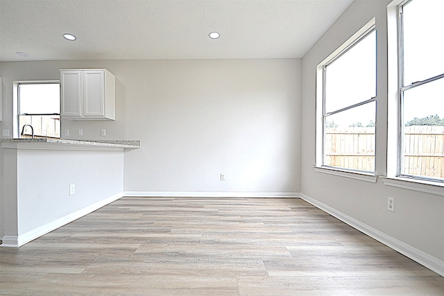 unfurnished dining area featuring sink, a textured ceiling, and light wood-type flooring