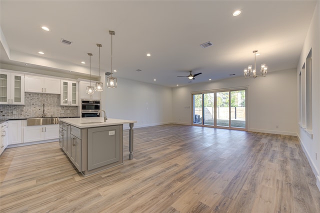 kitchen with ceiling fan with notable chandelier, sink, decorative light fixtures, a center island with sink, and a breakfast bar area