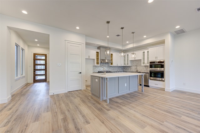 kitchen with pendant lighting, white cabinets, sink, light wood-type flooring, and an island with sink