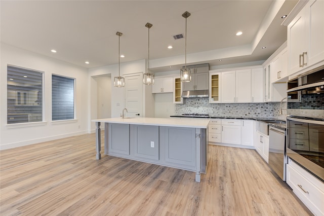 kitchen featuring stainless steel appliances, decorative light fixtures, light hardwood / wood-style flooring, white cabinetry, and an island with sink