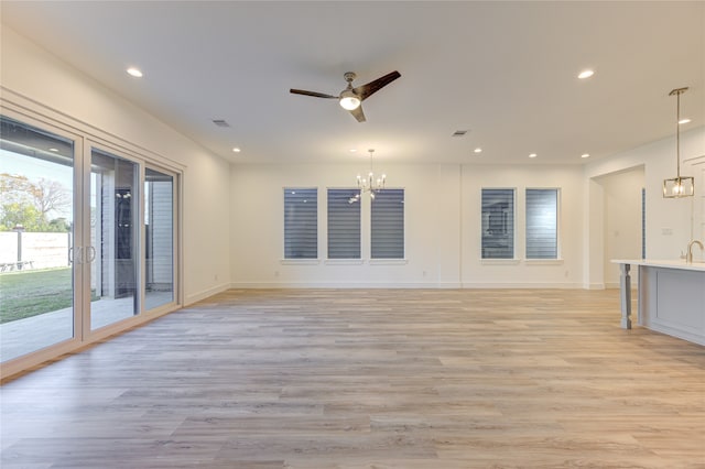 unfurnished living room with ceiling fan with notable chandelier and light hardwood / wood-style floors