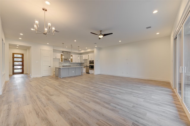 unfurnished living room featuring ceiling fan with notable chandelier and light wood-type flooring