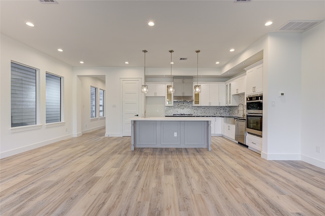 kitchen featuring white cabinets, decorative light fixtures, a kitchen island, and light hardwood / wood-style flooring