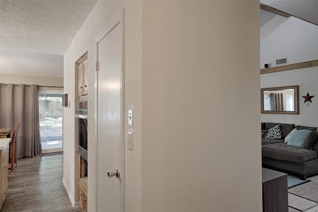 hall with light hardwood / wood-style floors, lofted ceiling, and a textured ceiling