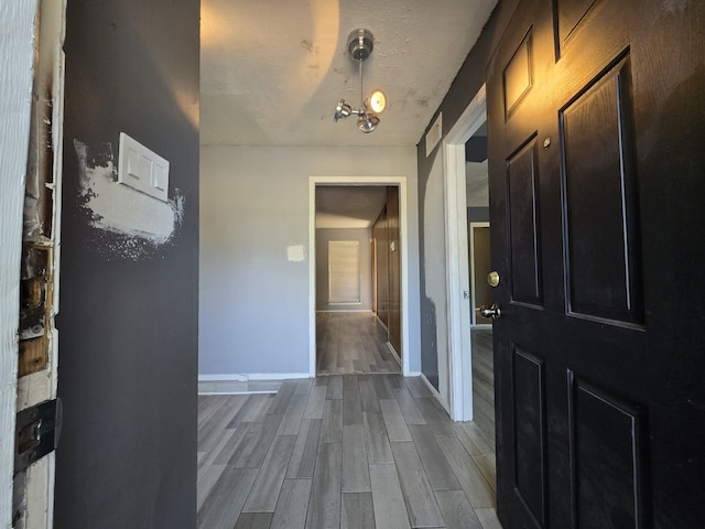 hallway featuring light wood-type flooring, a textured ceiling, and an inviting chandelier