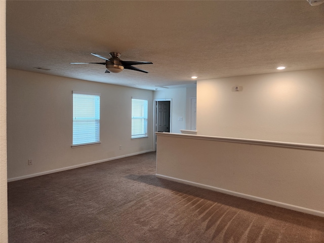 spare room featuring a textured ceiling, dark carpet, and ceiling fan