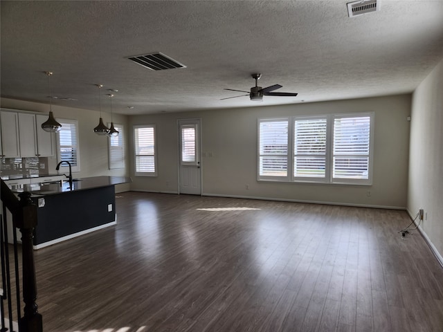 unfurnished living room featuring dark wood-type flooring, ceiling fan, a textured ceiling, and sink