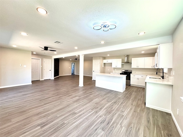 kitchen featuring wall chimney exhaust hood, stainless steel stove, sink, white cabinetry, and light hardwood / wood-style floors