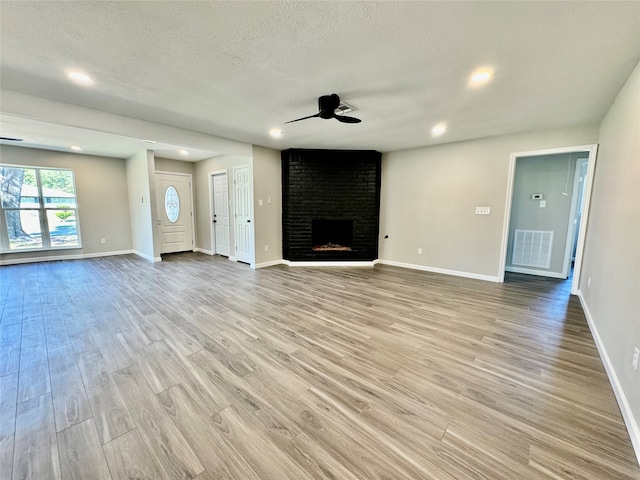 unfurnished living room with light hardwood / wood-style flooring, a textured ceiling, a fireplace, and ceiling fan