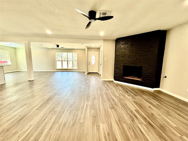 unfurnished living room with ceiling fan, a textured ceiling, light hardwood / wood-style flooring, and a fireplace