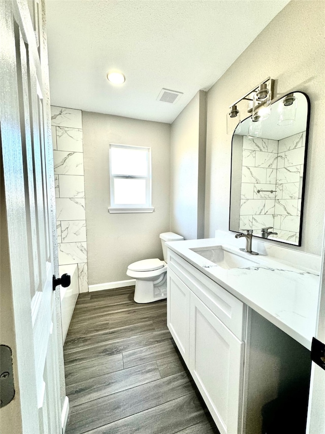 bathroom with tiled shower, toilet, hardwood / wood-style floors, vanity, and a textured ceiling